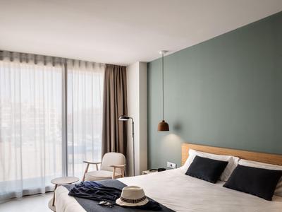 Modernes Hotelzimmer mit Doppelbett, Stuhl, großen Fenstern und grüner Akzentwand.