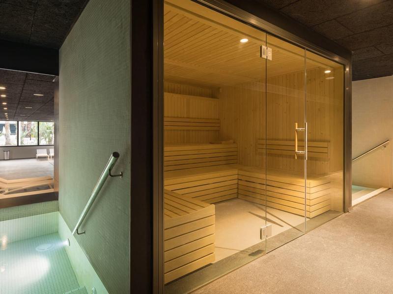 Modern sauna room with wooden benches and glass door beside a water pool area.