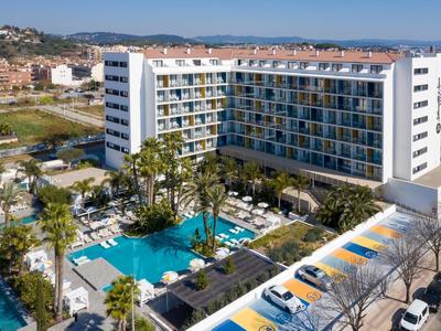 Großes Hotelgebäude mit vielen Balkonen, mehreren Schwimmbädern und Palmen im Außenbereich.
