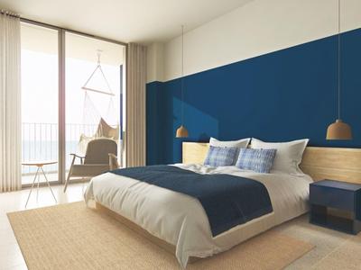 Gemütliches Schlafzimmer mit großem Bett, blauer Wand, Holzboden und natürlichem Licht.