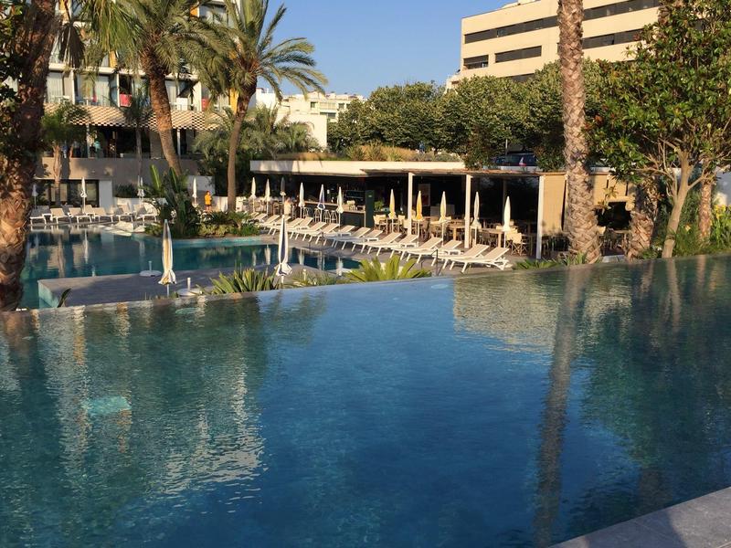 Outdoor hotel pool with sun loungers and umbrellas under clear sky.