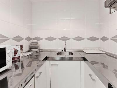 Cucina moderna con microonde, lavandino e piastrelle bianco-grigie in una camera d'hotel.