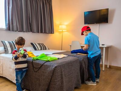 Due ragazzi giocano in una camera d'albergo con letto, TV e lampada da terra.