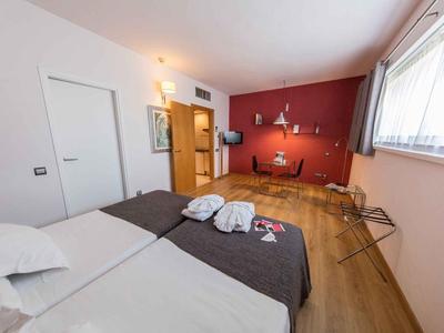 Modernes Hotelzimmer mit Doppelbett, roter Akzentwand, Schreibtisch und großem Fenster.