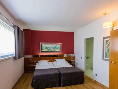 Hotelzimmer mit zwei Einzelbetten, Holzboden, roter Wand und großem Fenster mit Vorhängen.