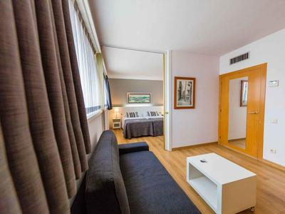 Modern eingerichtetes Hotelzimmer mit Sofa, Bett und hellen Holzmöbeln.