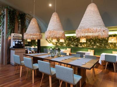 Moderní jídelní prostor s velkými dřevěnými lampami, modrými židlemi a dřevěnou podlahou v hotelové restauraci