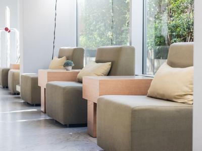 Moderní posezení s pohodlnými křesly, malými dřevěnými stolky a velkými okny s výhledem do zeleně.