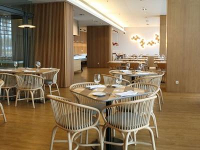 Modern hotel dining area with wooden tables, wicker chairs, and large windows offering natural light.