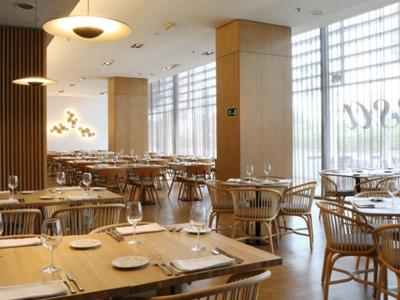 Bright hotel dining area with wooden chairs, neatly set tables, and large windows allowing ample sunlight.