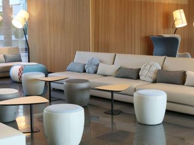 Modern hotel lounge area with white sofas, round ottomans, small black tables, and warm wooden walls.