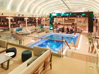 Salon moderne d'hôtel avec bar, coin salon et piscine intérieure éclairée sous un plafond voûté.