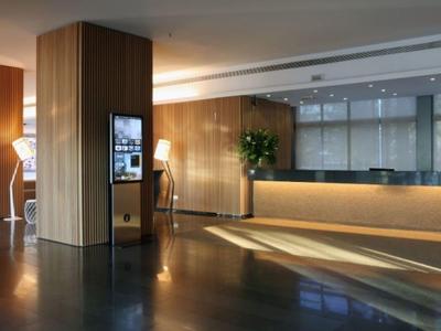 Modernes Hotel-Empfangsbereich mit hellem Holz, Beleuchtung und grünen Pflanzen, klare Linien.