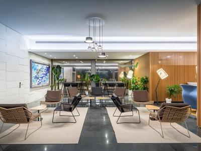 Hall d'hôtel moderne avec fauteuils, tapis et plantes.