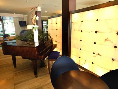 Moderner Raum mit Flügelklavier, gelb leuchtender Wand und runden Holzstühlen.