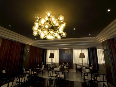 Eleganter Gastraum mit runden Tischen, Stühlen, großen Fenstern und goldener Kronleuchter-Deckenleuchte.