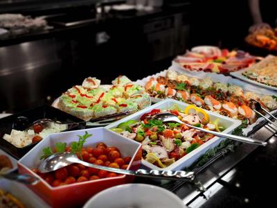 Vielfältige bunte Salate und Vorspeisen auf einem Buffet in weißen Schalen, beleuchtet.