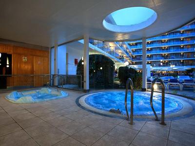 Innenbereich mit zwei beleuchteten, runden Pools, Holz- und Glaswände, blaue Akzente und Skylight.