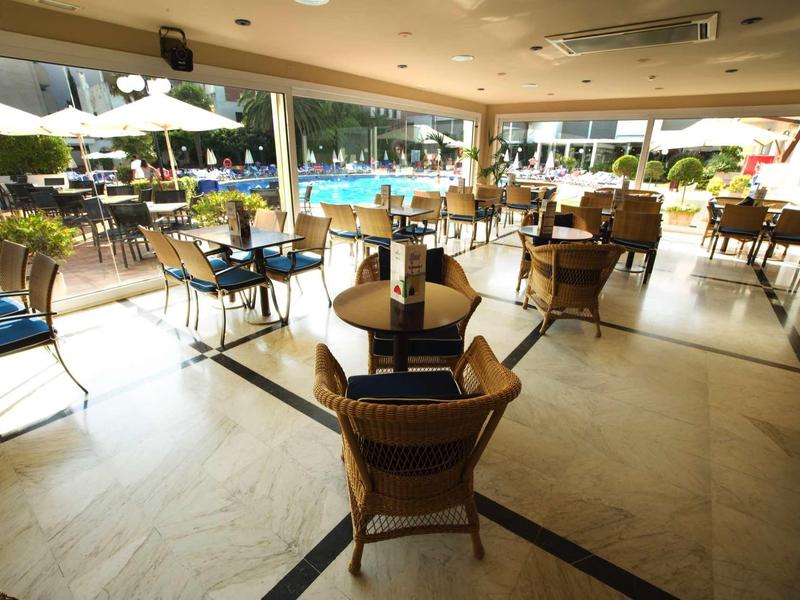Große helle Terrasse mit runden Tischen, Stühlen und Blick auf einen Pool und Garten.