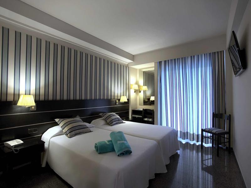 Modernes Hotelzimmer mit Doppelbett, gestreifter Wand, blauen Handtüchern und Vorhängen.