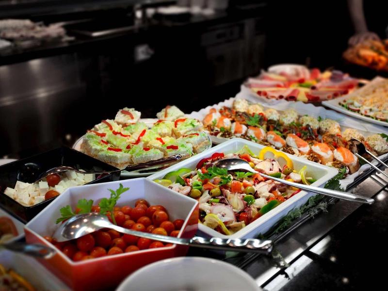 Vielfältige bunte Salate und Vorspeisen auf einem Buffet in weißen Schalen, beleuchtet.