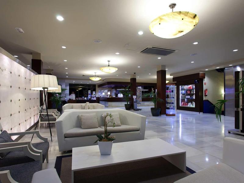 Moderne Lobby mit weißen Sofas, grauem Couchtisch, hohen Säulen und heller Deckenbeleuchtung.