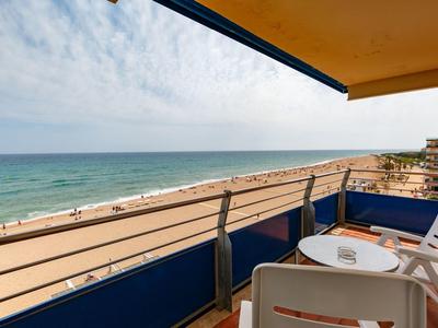 Balcón con sillas y mesa con vista a la playa de arena y el mar bajo un cielo nublado.
