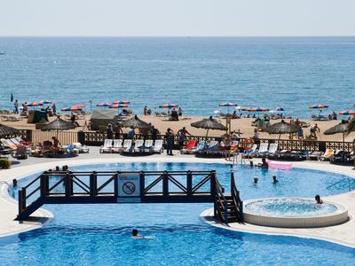 Vista de una playa con tumbonas, sombrillas y una piscina con un pequeño puente.