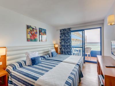 Habitación de hotel luminosa con cama doble, vista al mar y balcón, interior moderno.