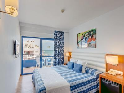 Habitación de hotel luminosa con cama doble, balcón y decoración en tonos azules y blancos.