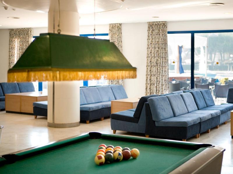 Área moderna de salón en hotel con mesa de billar, sofás azules y grandes ventanales