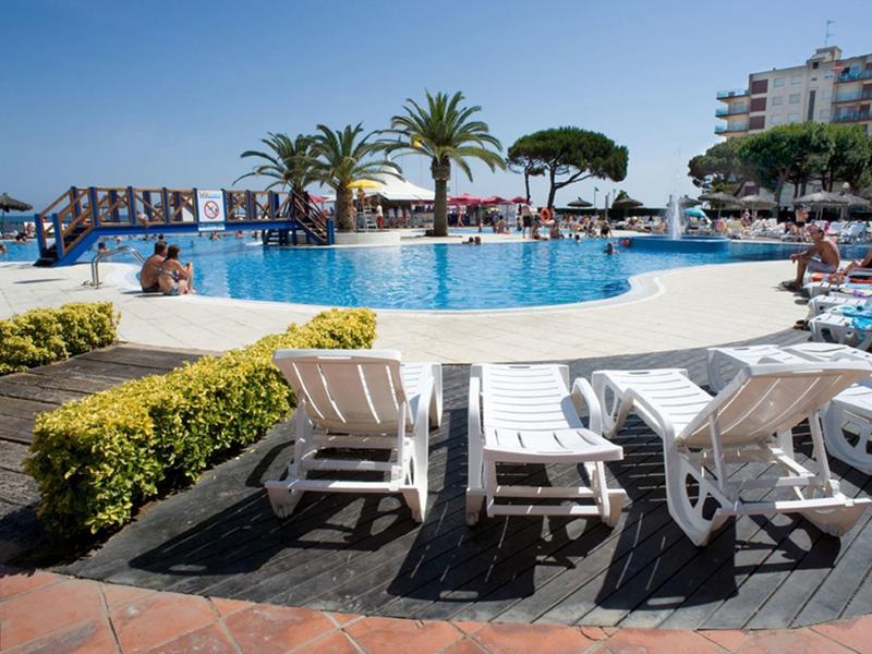 Piscina redonda del hotel con tumbonas, sombrillas y palmeras en un día soleado.