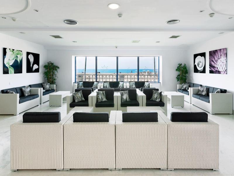 Salón moderno y luminoso con muebles blancos y vista al mar a través de grandes ventanales.