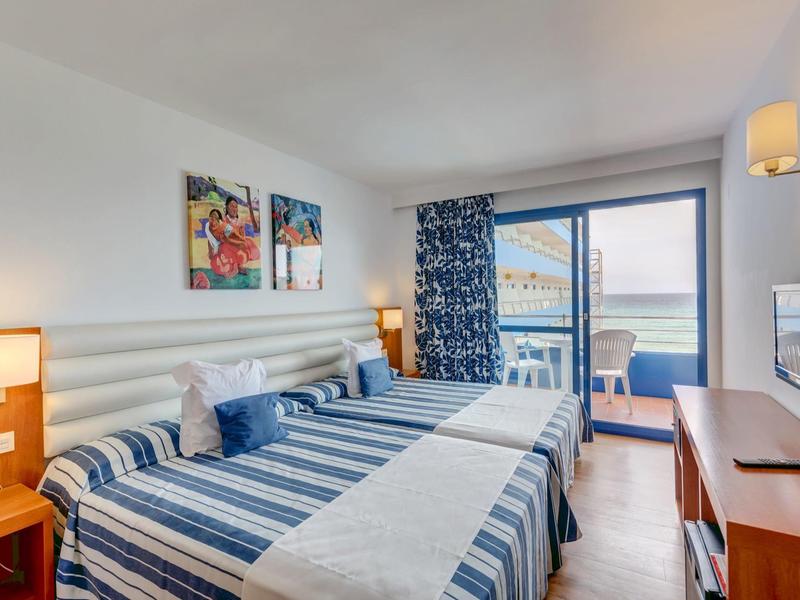 Habitación de hotel luminosa con cama doble, vista al mar y balcón, interior moderno.