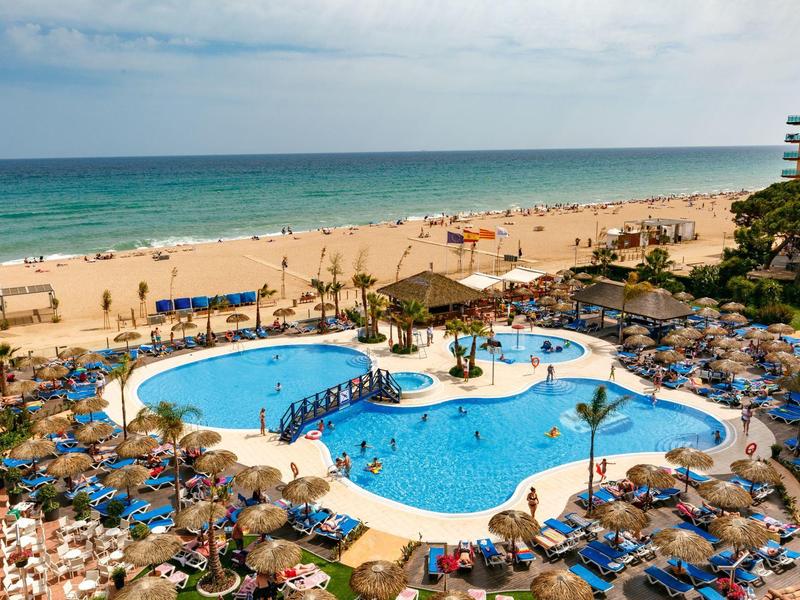 Piscina del hotel con muchas tumbonas en la playa con vistas al mar y la arena.