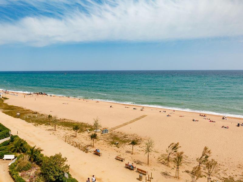 Amplia playa de arena con visitantes dispersos junto al mar azul claro bajo un cielo nublado.