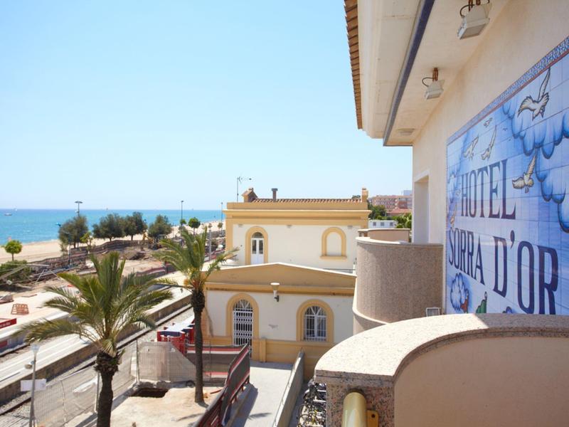 Vista de un hotel con vista al mar y palmeras en una carretera costera soleada.