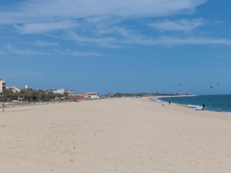 Amplia playa de arena con pocas personas y cielo azul en una costa.