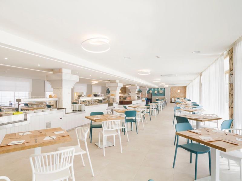 Restaurante moderno y luminoso con paredes blancas, sillas azules y blancas y grandes ventanas.