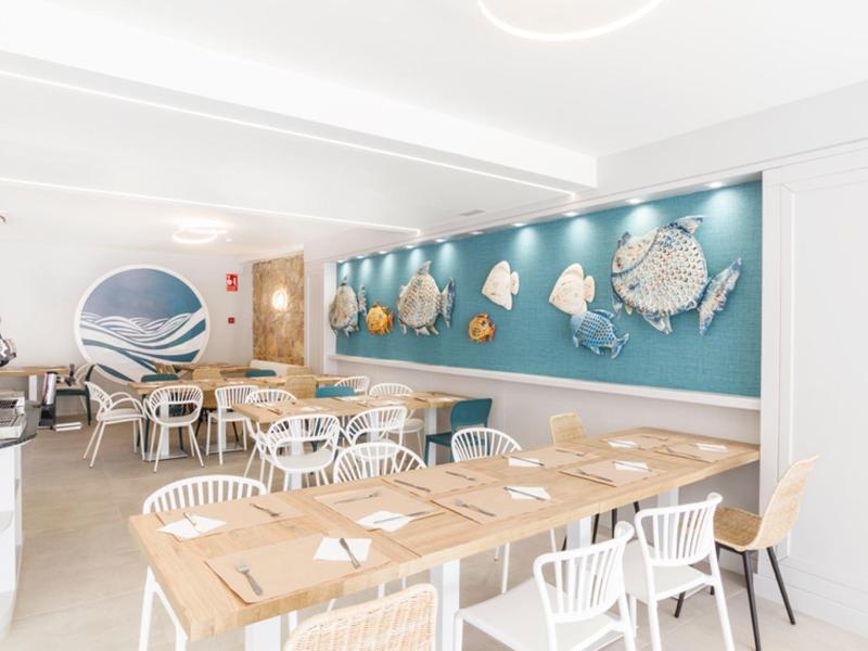 Restaurante moderno de hotel con sillas de madera y blancas, mesas y decoración marina en la pared.