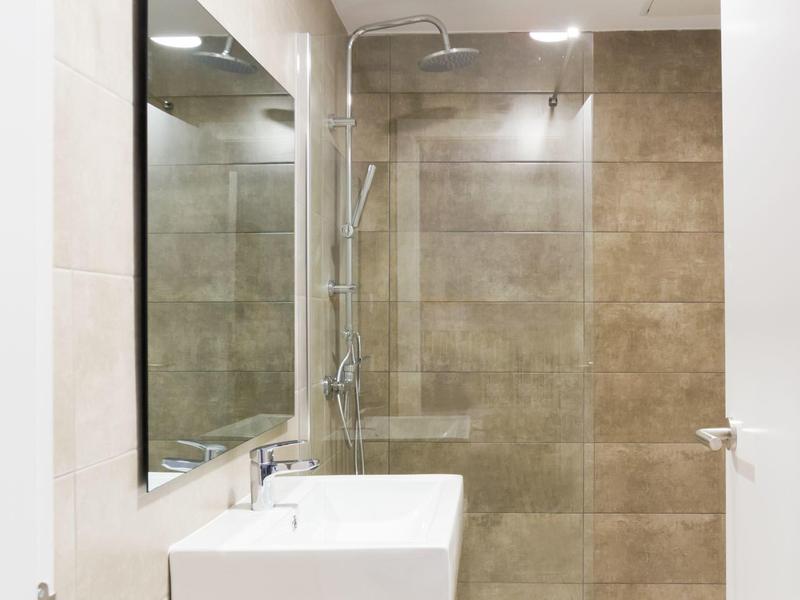 Baño moderno con lavabo blanco, espejo grande y ducha con azulejos beige.