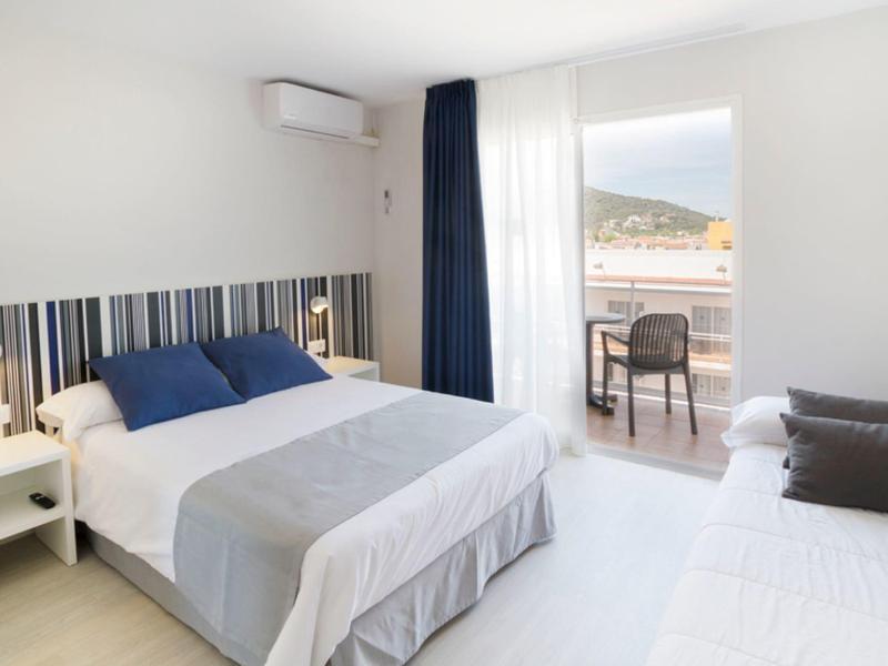 Habitación de hotel luminosa con cama doble, zona de estar y balcón con vistas a colinas.