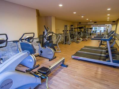 Moderner Fitnessraum mit Laufbändern, Fahrrädern und anderen Trainingsgeräten auf Holzboden.