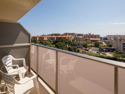 Balkon mit weißen Plastikstühlen und Blick auf Wohngebäude unter blauem Himmel.