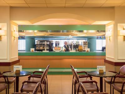 Gemütliche Bar mit Holzstühlen, Theke, Spiegel und drei Barkeepern im Hintergrund.