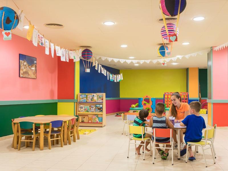 Sala giochi colorata per bambini con tavoli, sedie e decorazioni appese in un hotel.