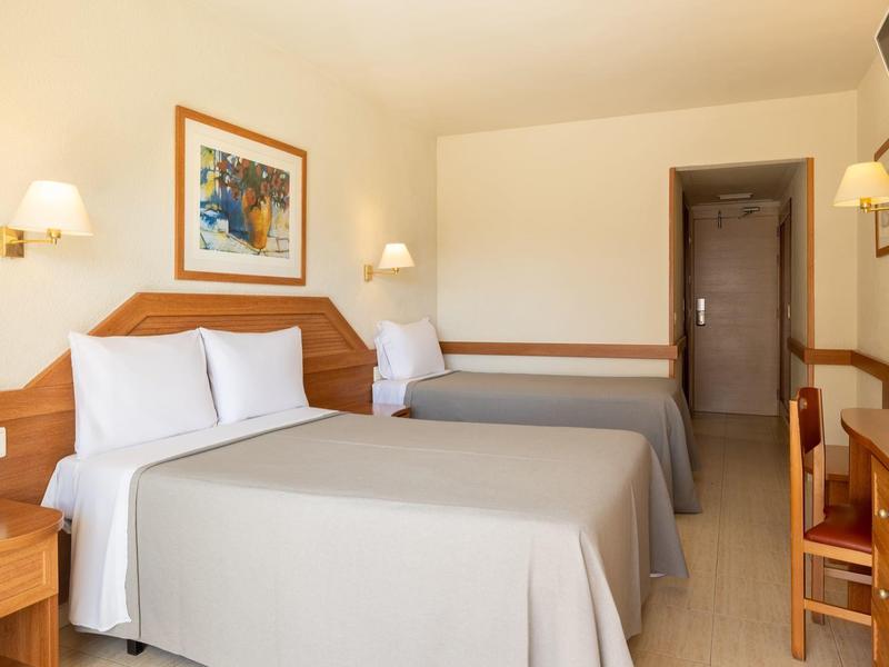 Camera d'hotel con due letti grandi, scrivania, sedia e illuminazione a parete luminosa.