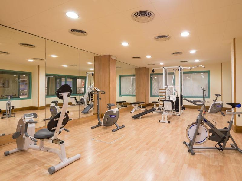 Palestra luminosa con varie attrezzature per esercizi e pareti a specchio.