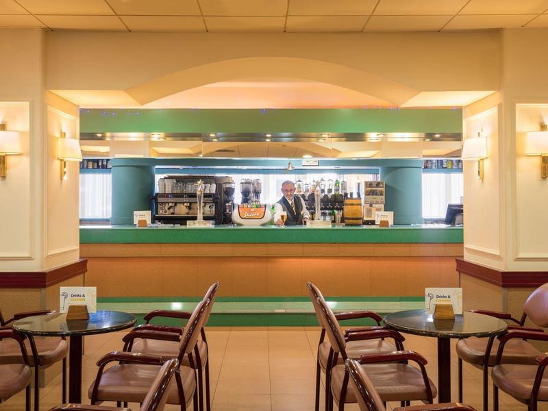 Bar dell'hotel moderno con bancone, sgabelli e aree salotto con illuminazione calda.