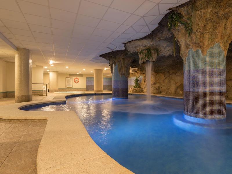 Piscina interna con design a roccia naturale e illuminazione soffusa in un hotel.